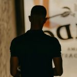 Back view of a man walking down dimly lit stairs indoors, creating a moody silhouette effect.